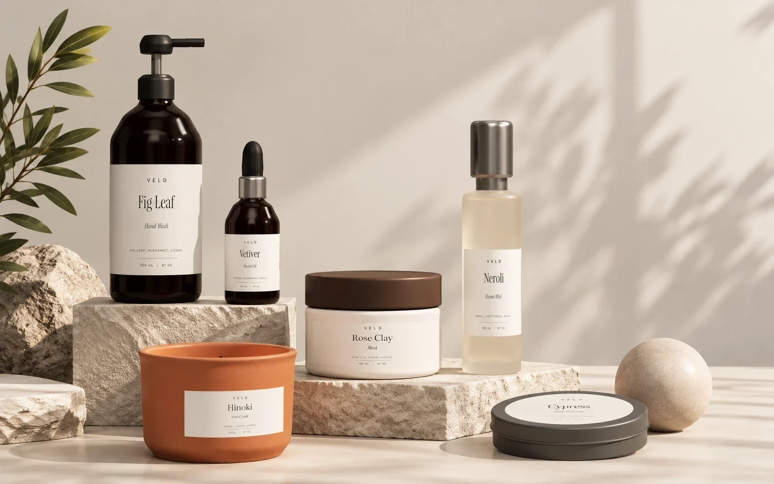 Veld still life on stone blocks: Fig Leaf hand wash, Vetiver facial oil, Rose Clay mask, Neroli room mist, a Hinoki candle, and a Cypress tin in warm light